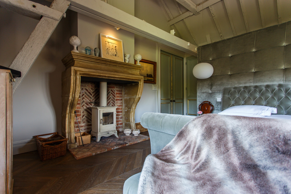 サセックスにある中くらいなコンテンポラリースタイルのおしゃれな寝室 (濃色無垢フローリング、薪ストーブ、レンガの暖炉まわり、茶色い床、ベージュの壁) のインテリア