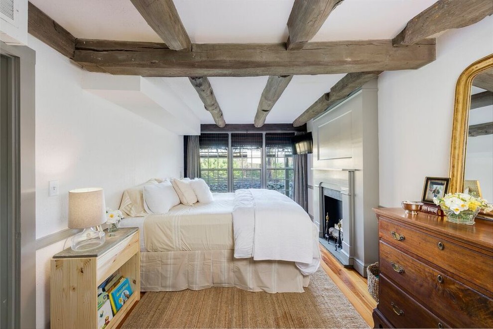 Imagen de dormitorio principal de estilo de casa de campo con todas las chimeneas, paredes blancas y suelo de madera en tonos medios