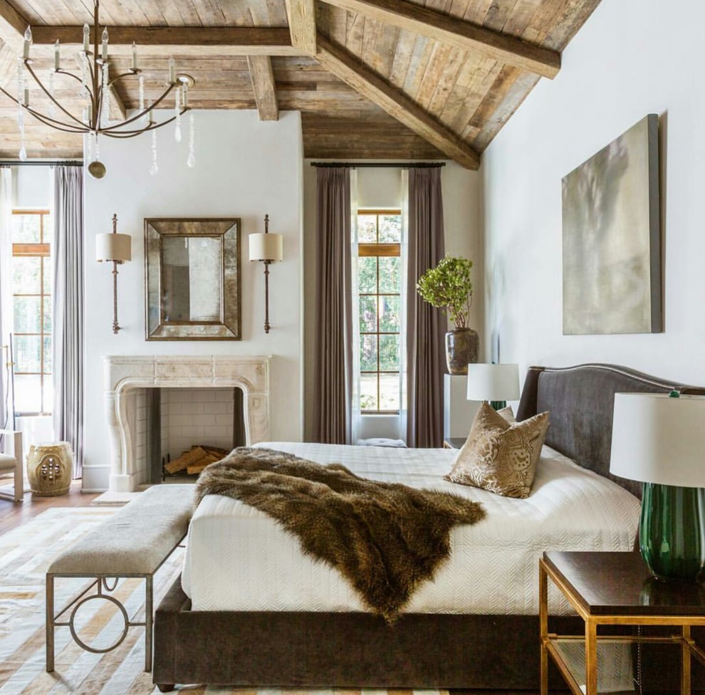 Modelo de dormitorio principal de estilo de casa de campo grande con paredes blancas, suelo de madera clara, todas las chimeneas, marco de chimenea de baldosas y/o azulejos y suelo beige