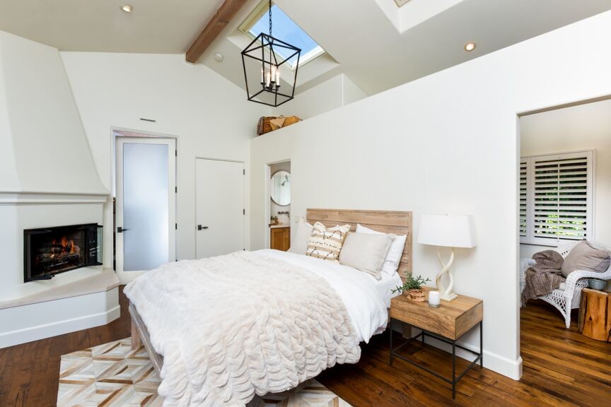 Ejemplo de dormitorio principal contemporáneo de tamaño medio con paredes blancas, suelo de madera en tonos medios, chimenea de esquina y marco de chimenea de yeso