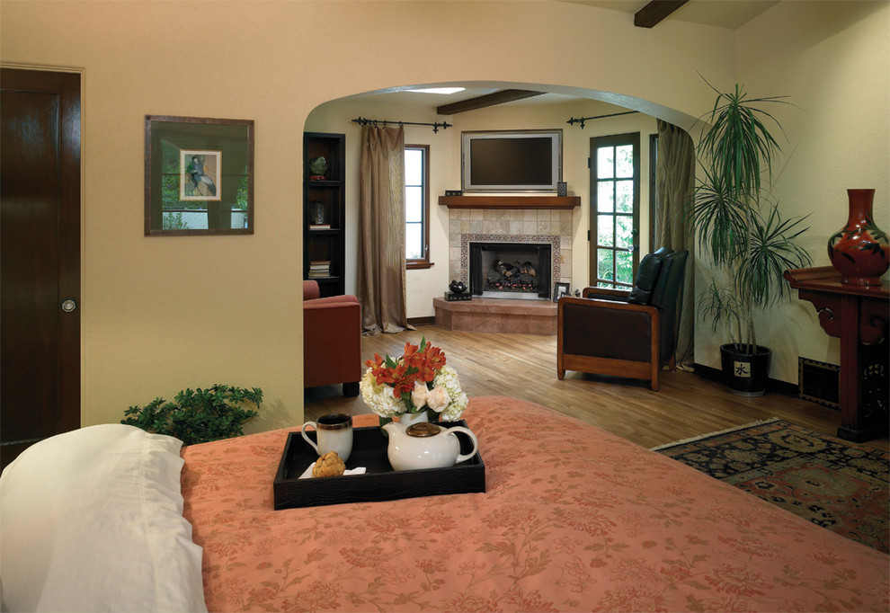 Exemple d'une chambre méditerranéenne avec un mur beige, un sol en bois brun, une cheminée d'angle et un manteau de cheminée en carrelage.