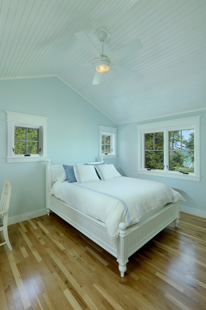 他の地域にある小さなカントリー風のおしゃれな客用寝室 (青い壁、淡色無垢フローリング、茶色い床)