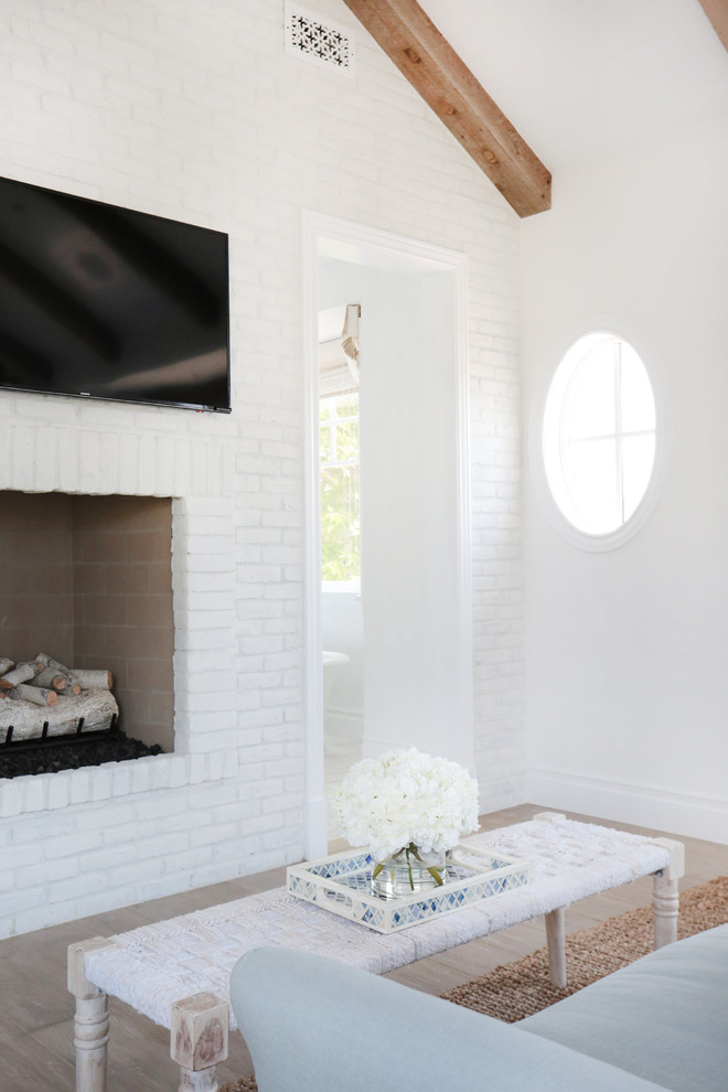 Photo of a medium sized coastal master bedroom in Orange County with white walls, light hardwood flooring, a standard fireplace and a brick fireplace surround.