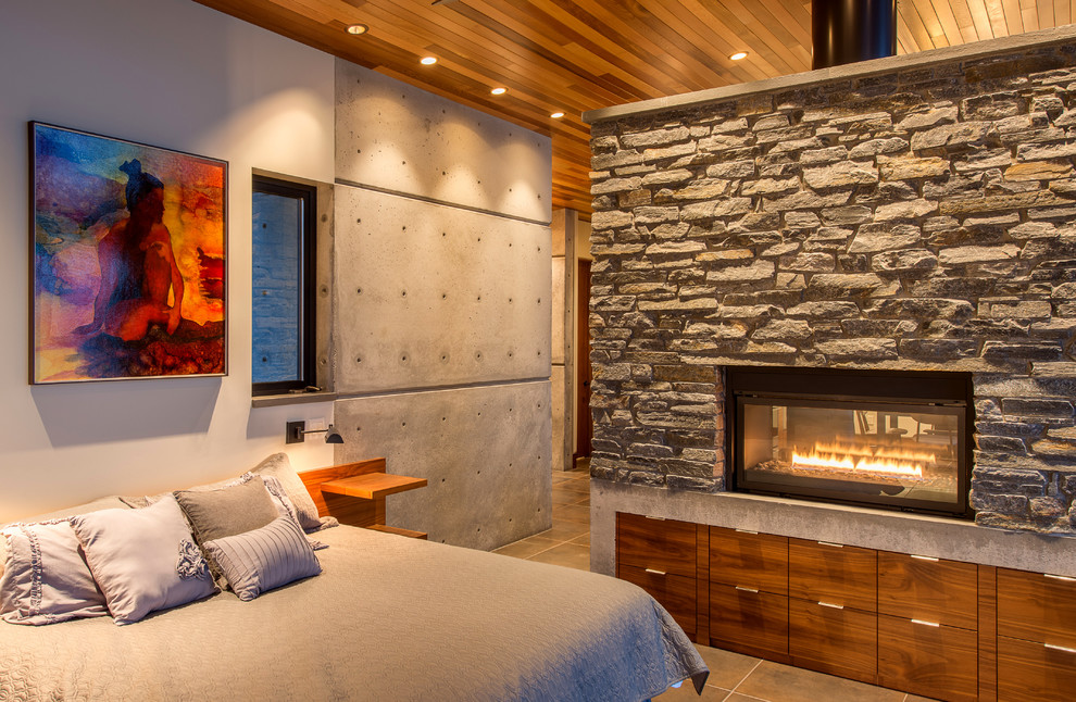 Immagine di una piccola camera da letto stile loft moderna con pareti bianche, pavimento in gres porcellanato, stufa a legna, cornice del camino in pietra e pavimento beige
