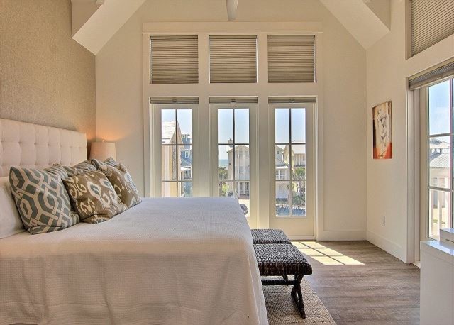 Modelo de dormitorio principal costero de tamaño medio con paredes blancas, suelo de madera en tonos medios y suelo marrón