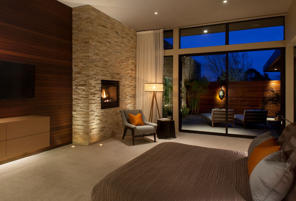На фото: спальня в современном стиле с ковровым покрытием и фасадом камина из камня с