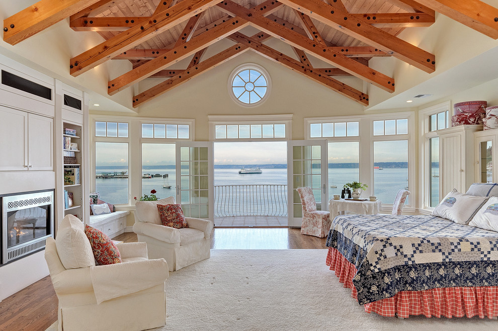 Large beach style master medium tone wood floor bedroom photo in Seattle with beige walls, a metal fireplace and a standard fireplace