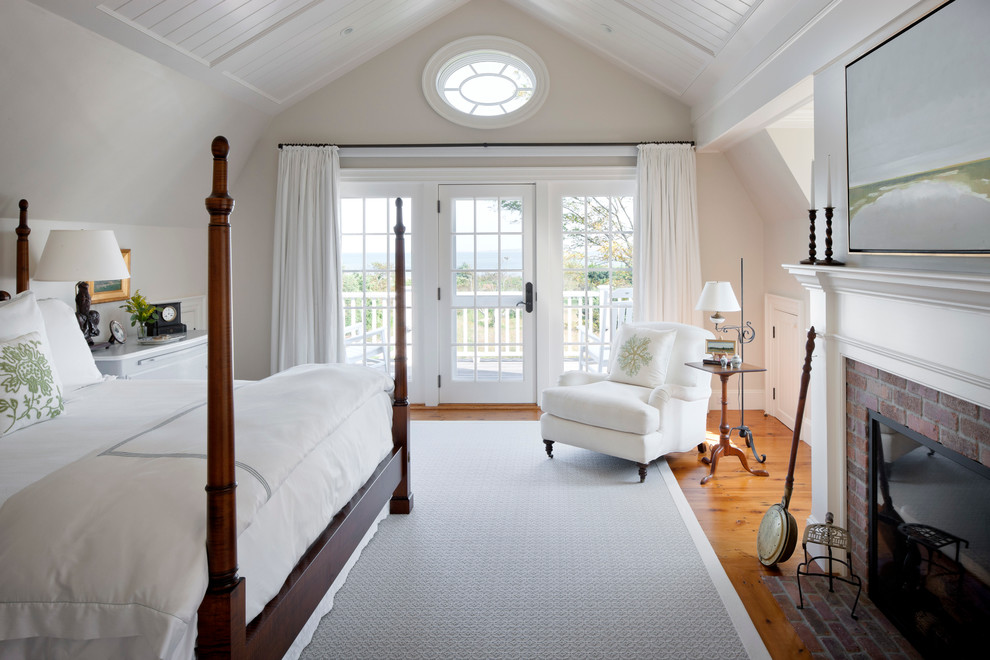 Foto di una camera da letto costiera con pareti beige, pavimento in legno massello medio, camino classico e cornice del camino in mattoni