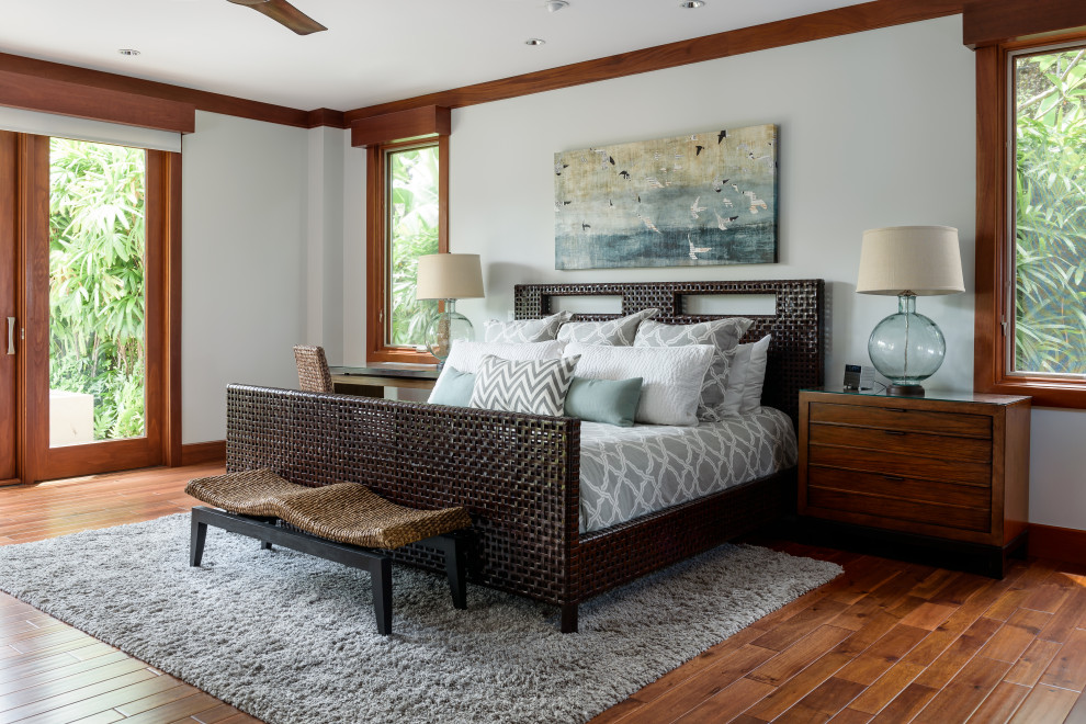 Ejemplo de dormitorio principal exótico sin chimenea con paredes blancas, suelo de madera en tonos medios, suelo marrón y con escritorio