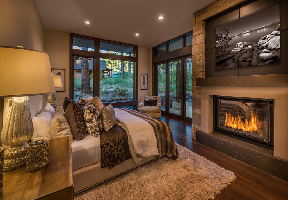 Mountain style dark wood floor and brown floor bedroom photo in Other with beige walls and a standard fireplace