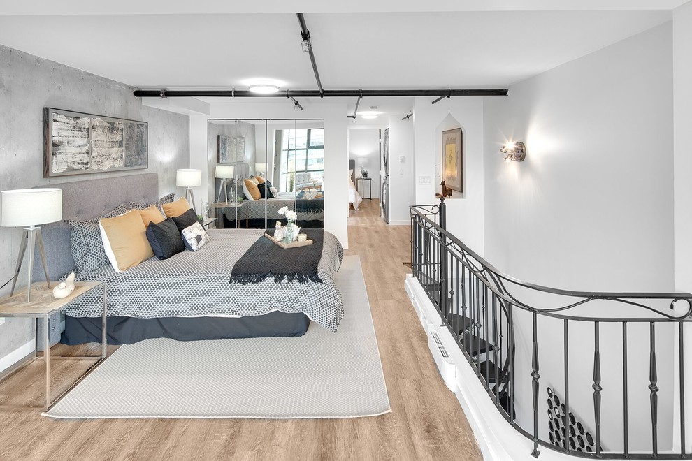 Imagen de dormitorio tipo loft urbano sin chimenea con paredes grises y suelo de madera clara