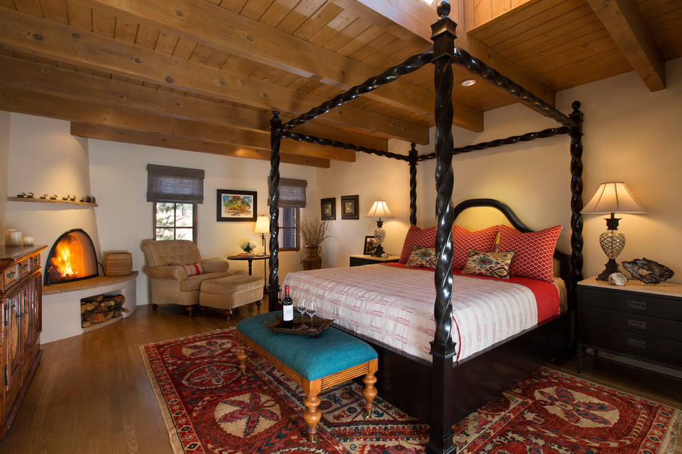 Idée de décoration pour une chambre parentale sud-ouest américain avec un mur blanc, un sol en bois brun et une cheminée d'angle.