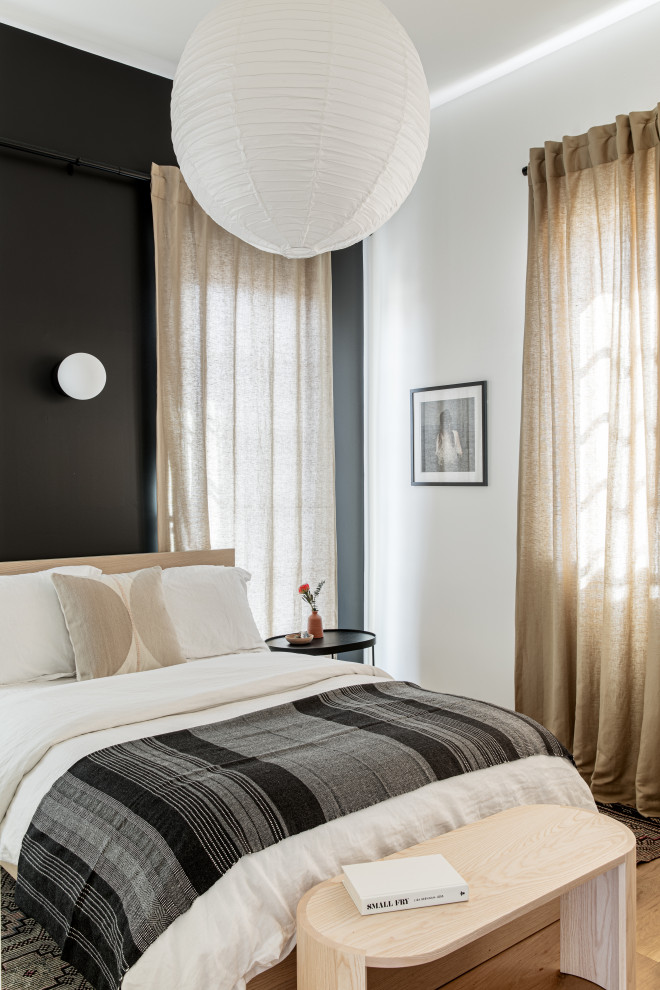 This is an example of a small scandi cream and black bedroom in New York with black walls, light hardwood flooring and no fireplace.