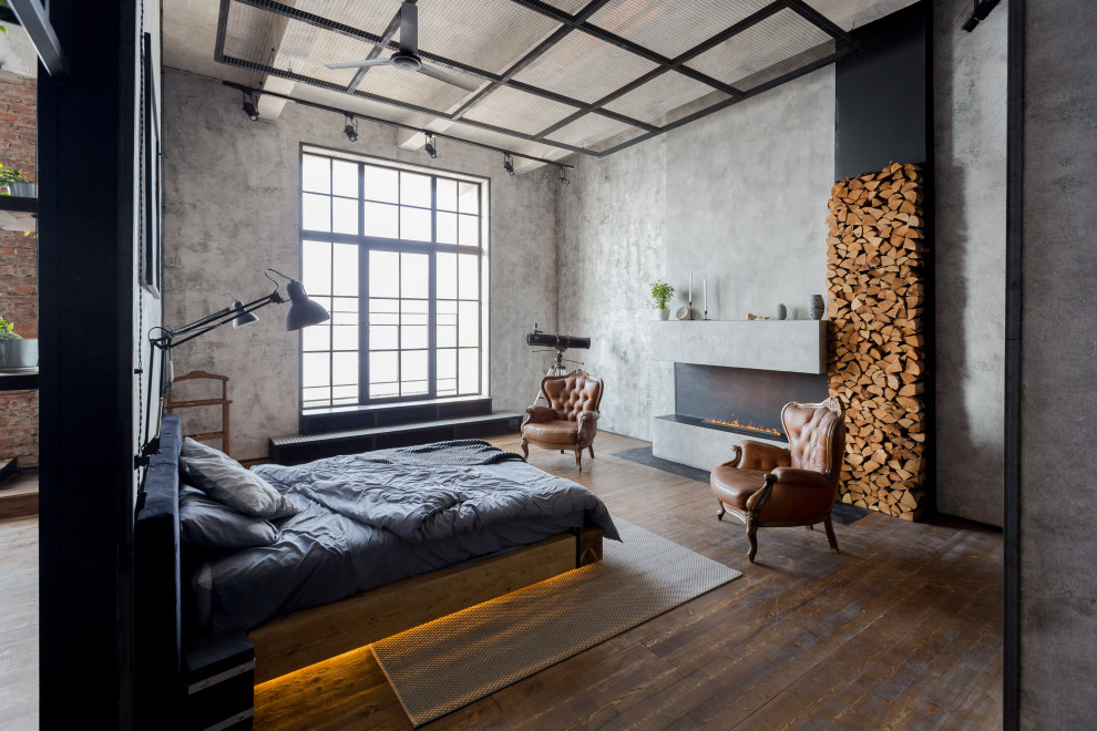 Inspiration för ett industriellt sovrum, med grå väggar, mörkt trägolv, en bred öppen spis och brunt golv