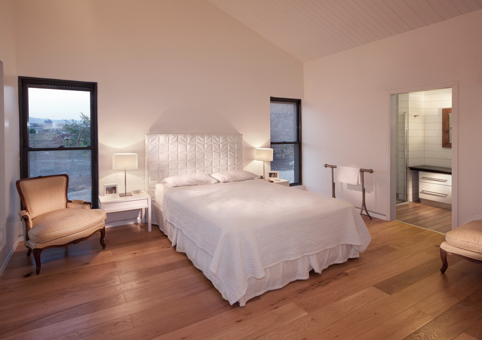 Immagine di una camera da letto design con pareti bianche, pavimento in legno massello medio e nessun camino