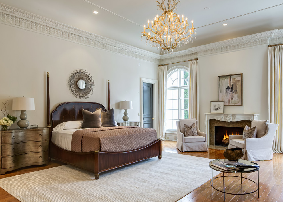 Klassisches Hauptschlafzimmer mit beiger Wandfarbe, braunem Holzboden, Kamin und Kaminumrandung aus Stein in Atlanta