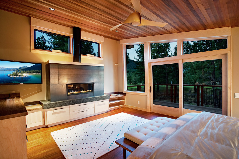 Imagen de dormitorio principal y televisión rural de tamaño medio con suelo de madera en tonos medios, chimenea lineal, paredes negras y marco de chimenea de metal
