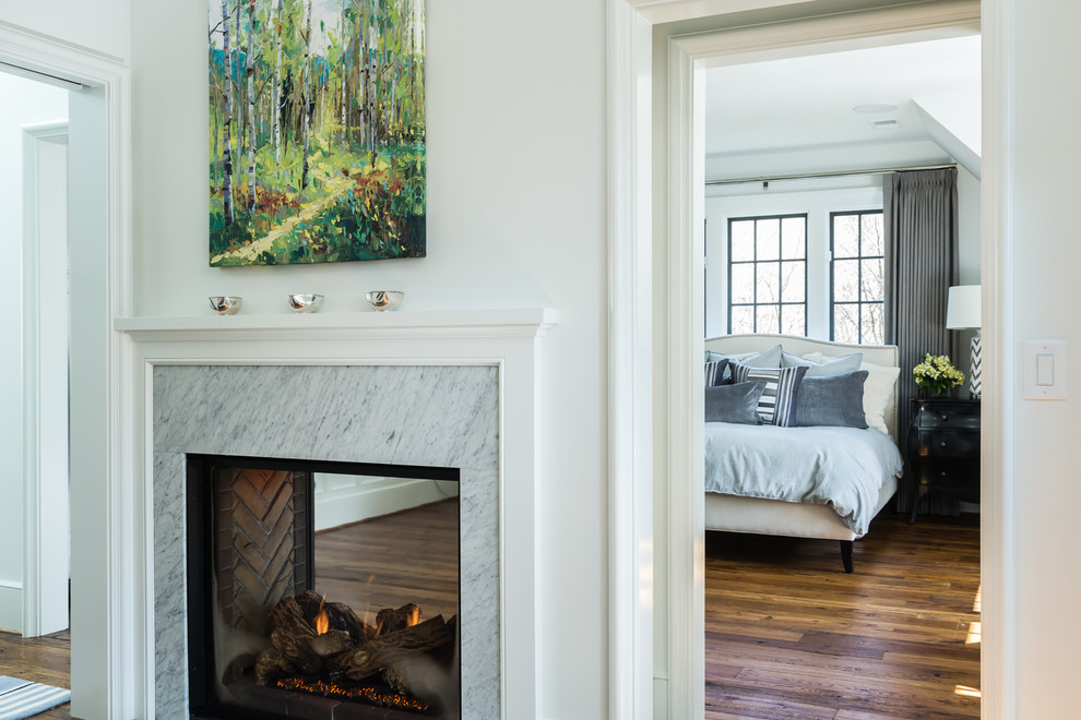 Cette photo montre une chambre parentale tendance avec un mur blanc, un sol en bois brun, une cheminée double-face et un manteau de cheminée en pierre.