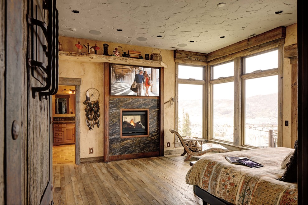 Bedroom - mid-sized rustic master light wood floor bedroom idea in Minneapolis with beige walls, a two-sided fireplace and a stone fireplace