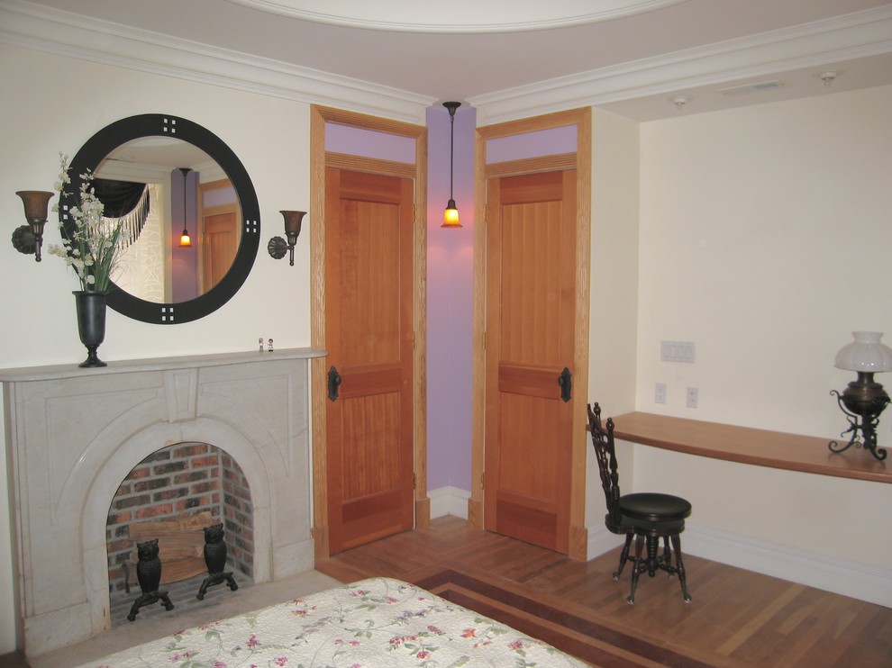 Modelo de habitación de invitados tradicional de tamaño medio con paredes púrpuras, suelo de madera clara, todas las chimeneas y marco de chimenea de piedra