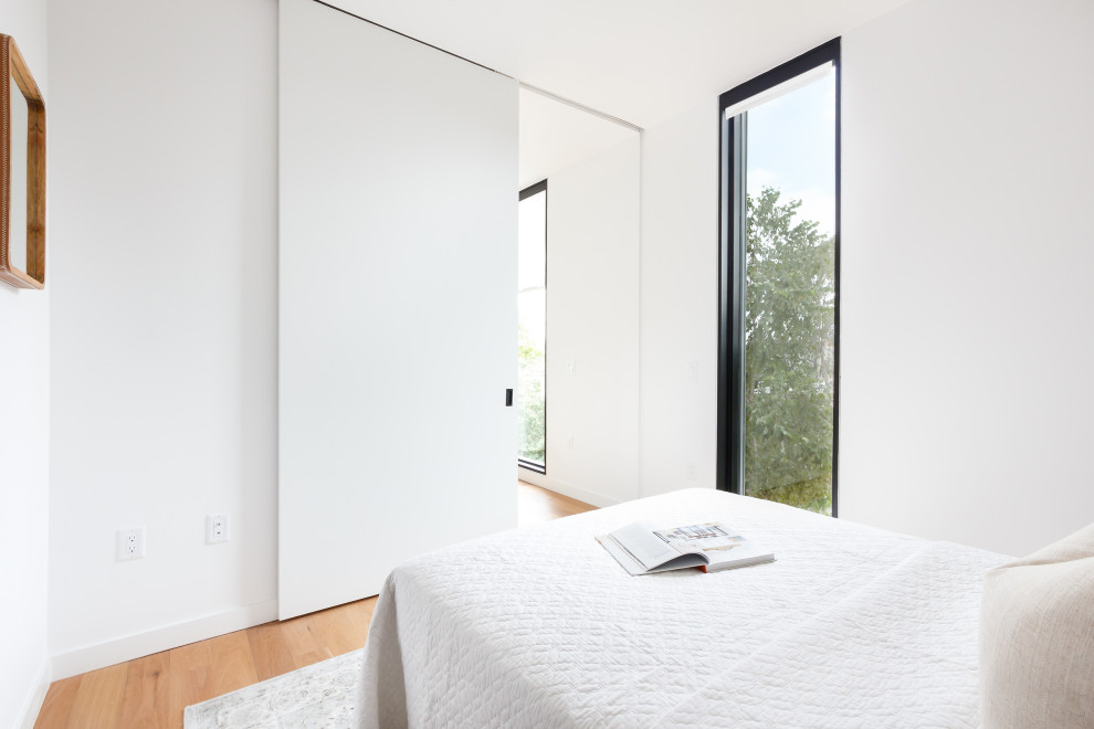 Foto de habitación de invitados minimalista con paredes blancas, suelo de madera en tonos medios y suelo marrón