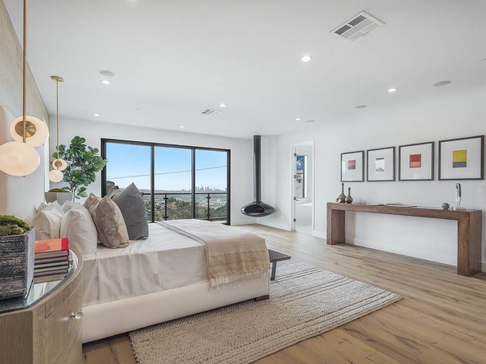 Geräumiges Retro Hauptschlafzimmer mit Hängekamin, weißer Wandfarbe, hellem Holzboden und braunem Boden in Los Angeles