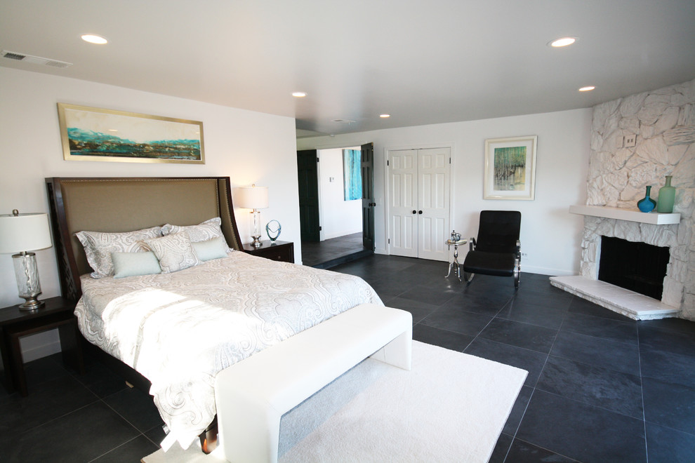 На фото: хозяйская спальня среднего размера в стиле модернизм с белыми стенами, полом из сланца, угловым камином и фасадом камина из камня с