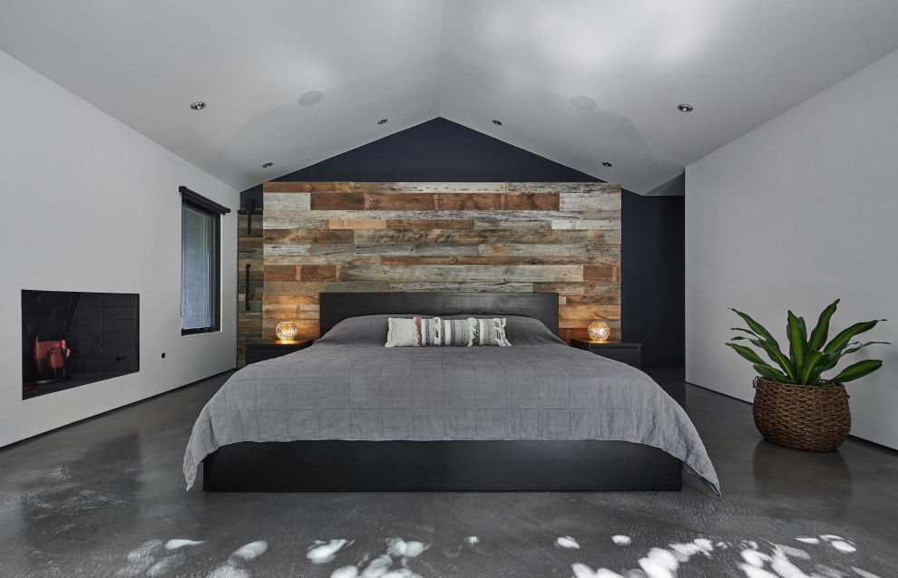 На фото: большая хозяйская спальня в стиле ретро с белыми стенами, бетонным полом, стандартным камином, фасадом камина из штукатурки и серым полом с