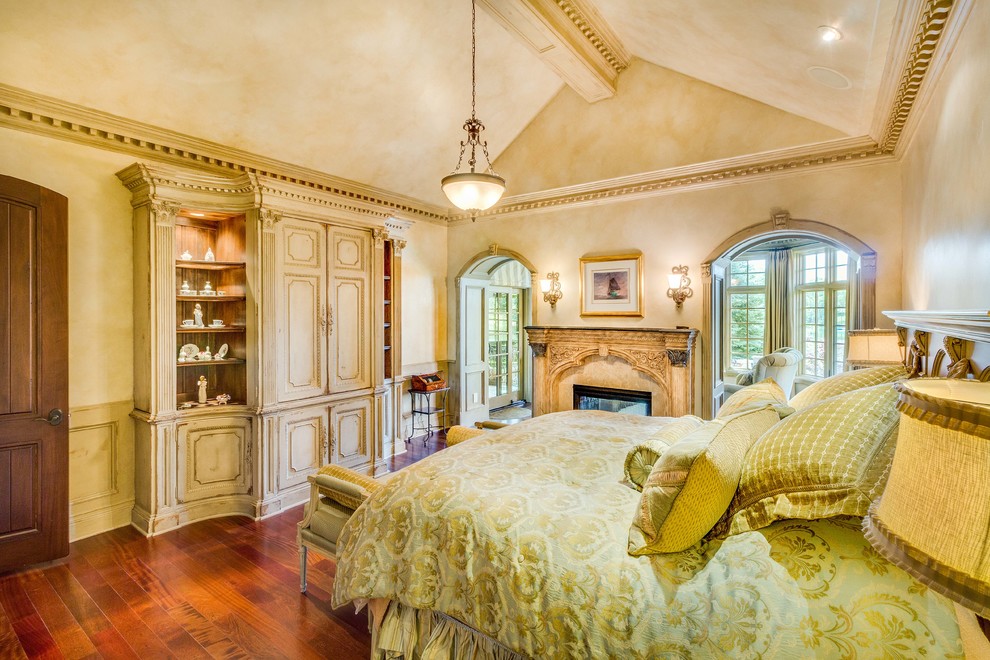 Inspiration pour une grande chambre parentale traditionnelle avec un mur beige, un sol en bois brun, une cheminée double-face, un manteau de cheminée en plâtre et un sol marron.