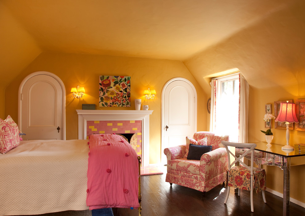 Klassisches Schlafzimmer im Dachboden mit gelber Wandfarbe, dunklem Holzboden, Kamin und gefliester Kaminumrandung in Los Angeles