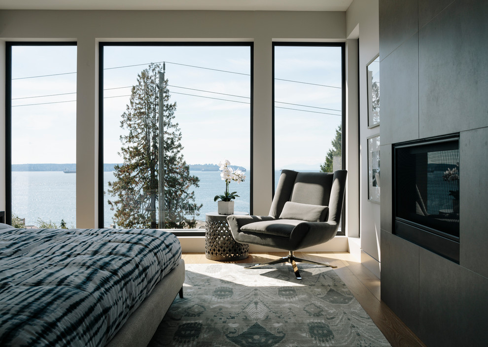 This is an example of a large contemporary master bedroom in Vancouver with white walls, medium hardwood flooring, a two-sided fireplace and a tiled fireplace surround.