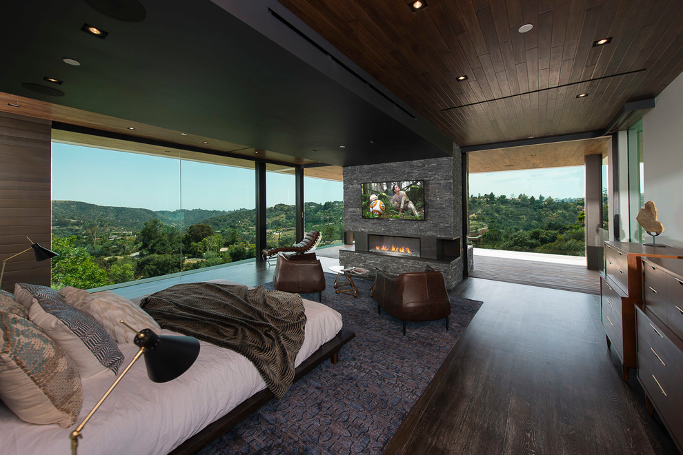 Modernes Schlafzimmer mit brauner Wandfarbe, dunklem Holzboden, Gaskamin, Kaminumrandung aus Stein und braunem Boden in Los Angeles