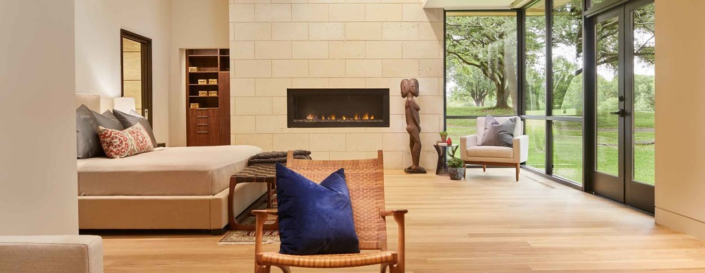 Example of a large minimalist master medium tone wood floor and brown floor bedroom design in Dallas with beige walls, a ribbon fireplace and a stone fireplace