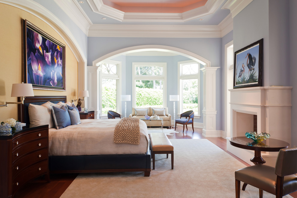 Idée de décoration pour une très grande chambre parentale tradition avec un mur bleu, un sol en bois brun, une cheminée standard, un manteau de cheminée en bois et un sol marron.