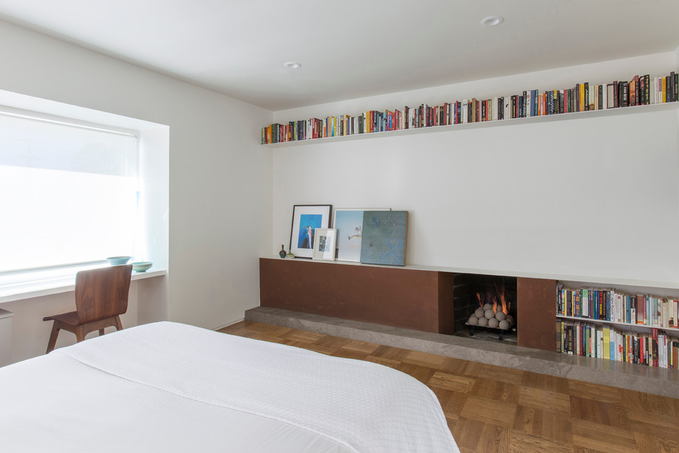 Cette image montre une chambre d'amis design de taille moyenne avec un mur blanc, un sol en bois brun, une cheminée standard et un manteau de cheminée en métal.