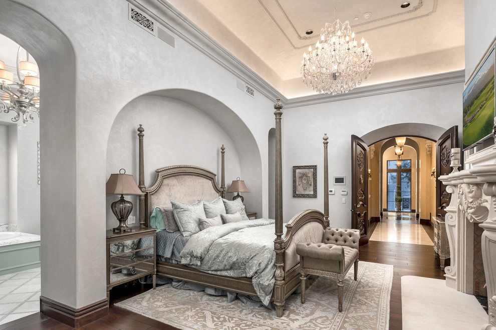 На фото: большая хозяйская спальня в стиле модернизм с серыми стенами, паркетным полом среднего тона, двусторонним камином, фасадом камина из камня и коричневым полом