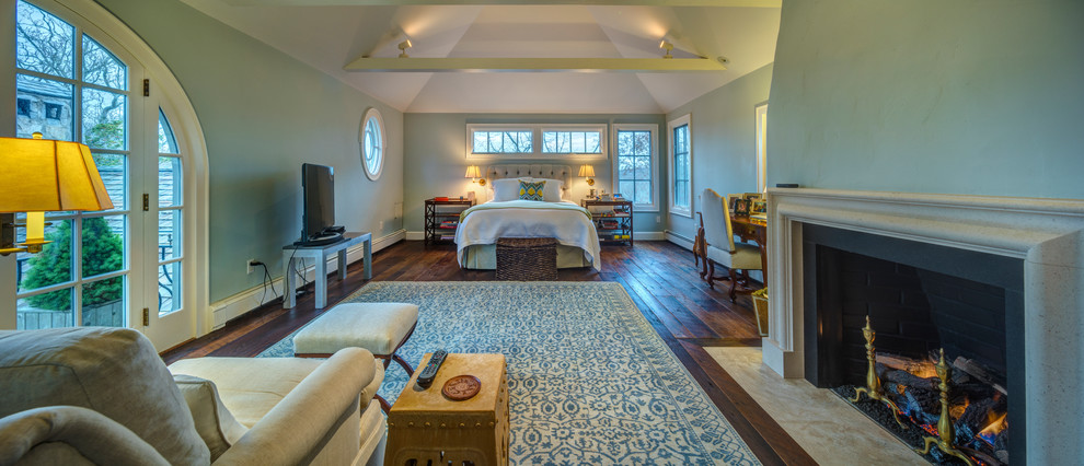 ニューヨークにある広い地中海スタイルのおしゃれな主寝室 (青い壁、無垢フローリング、標準型暖炉、漆喰の暖炉まわり、茶色い床) のインテリア