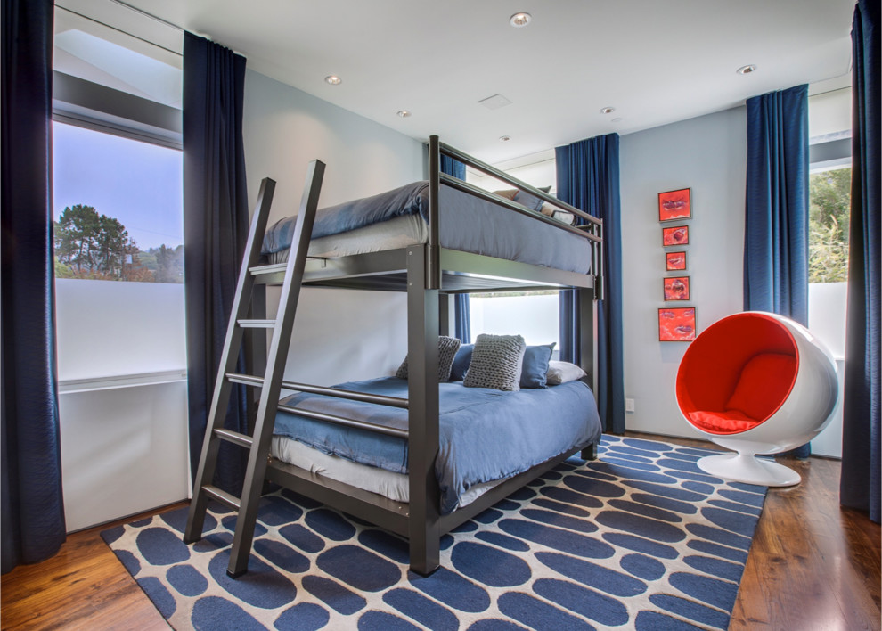 Modelo de habitación de invitados actual grande sin chimenea con paredes azules y suelo de madera en tonos medios