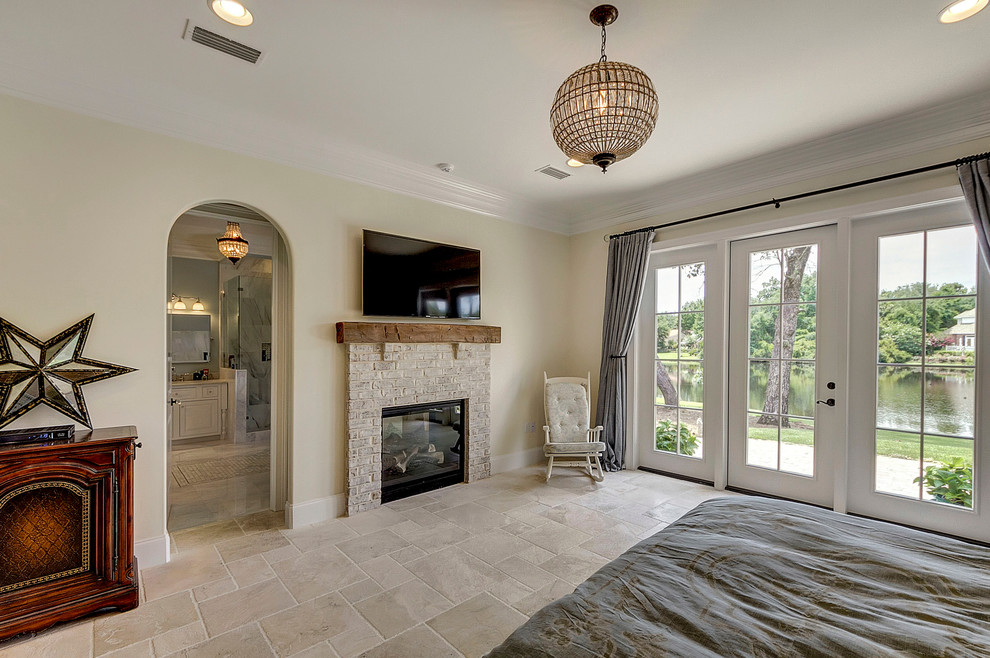 Aménagement d'une grande chambre parentale classique avec un mur beige, un sol en travertin, une cheminée double-face et un manteau de cheminée en brique.