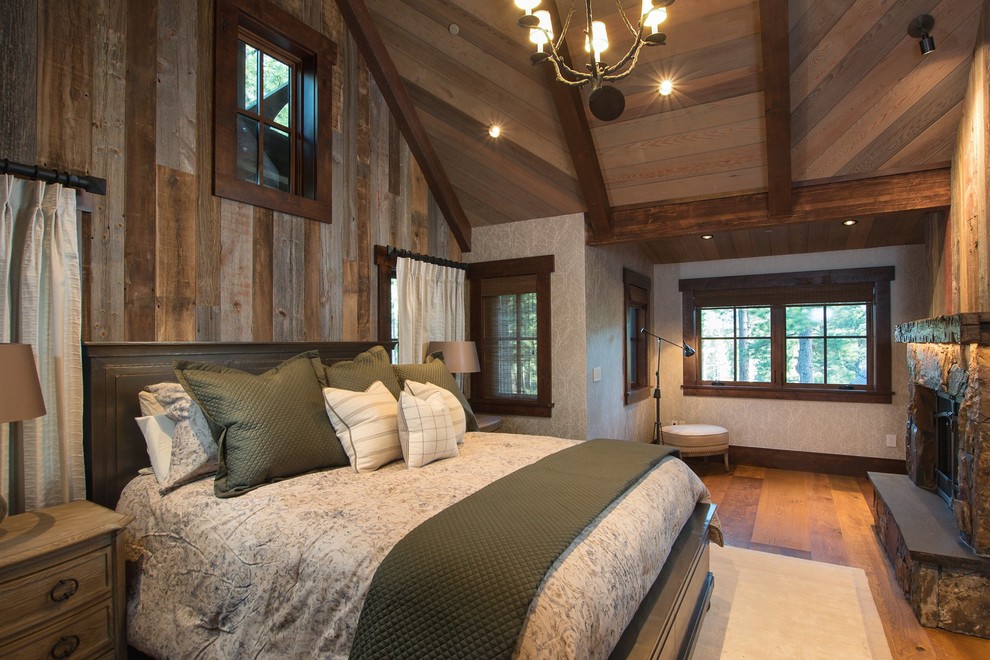 Ejemplo de dormitorio principal rústico con suelo de madera en tonos medios y marco de chimenea de piedra