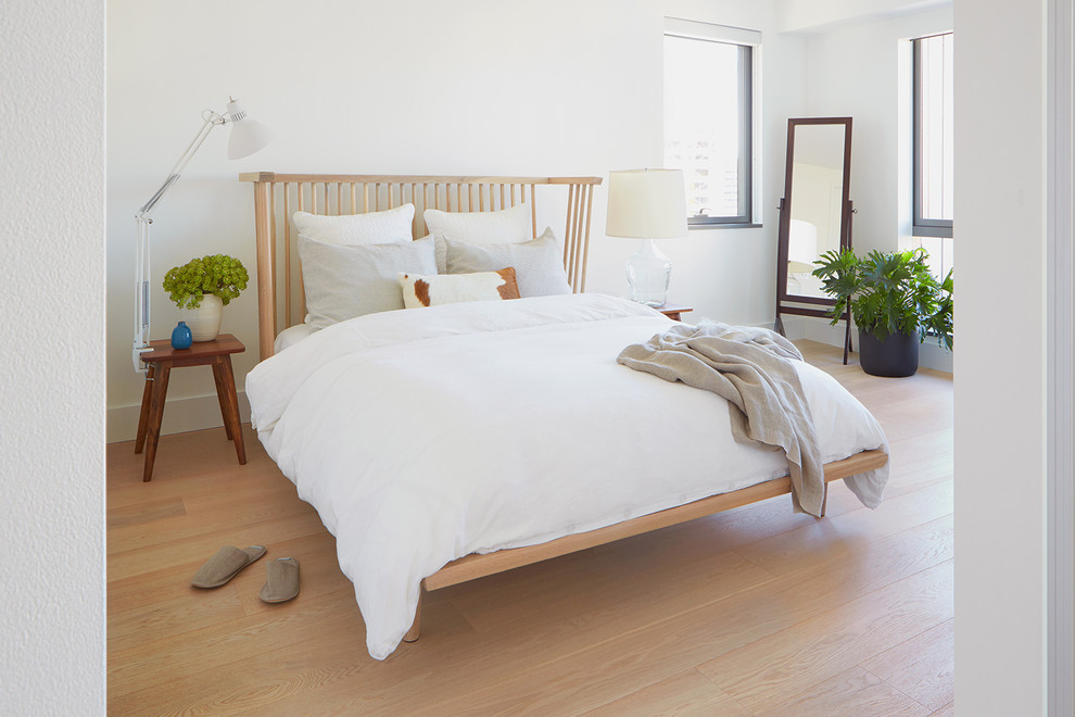 Imagen de dormitorio principal escandinavo pequeño con paredes blancas, suelo de madera clara, chimenea de doble cara, marco de chimenea de piedra y suelo beige