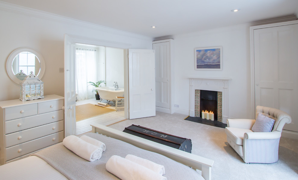 Geräumiges Modernes Hauptschlafzimmer mit weißer Wandfarbe, Teppichboden, Kamin und gefliester Kaminumrandung in Cornwall