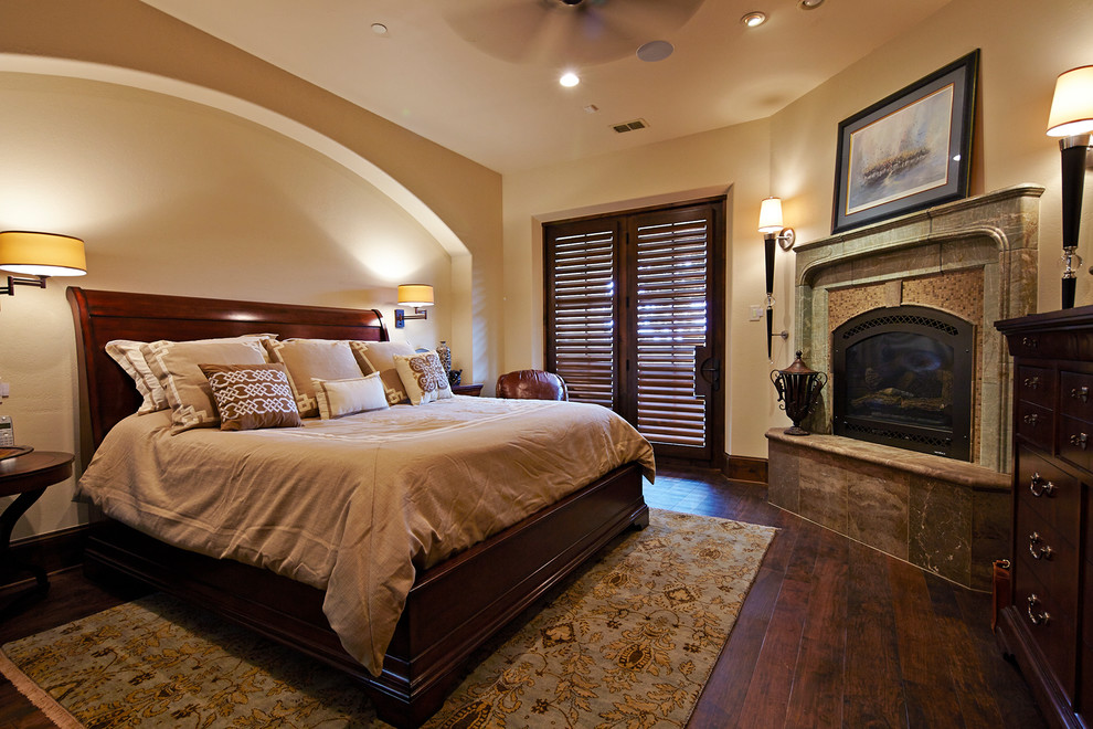 Großes Klassisches Hauptschlafzimmer mit beiger Wandfarbe, dunklem Holzboden, Kamin und gefliester Kaminumrandung in Austin