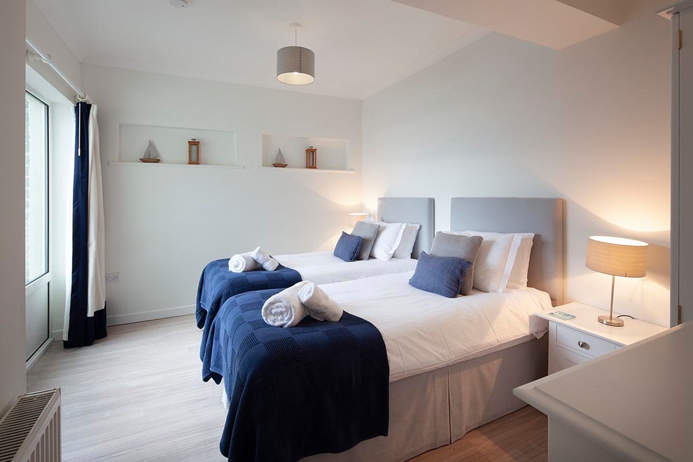 This is an example of a medium sized beach style guest bedroom in Cornwall with white walls, light hardwood flooring, no fireplace and beige floors.