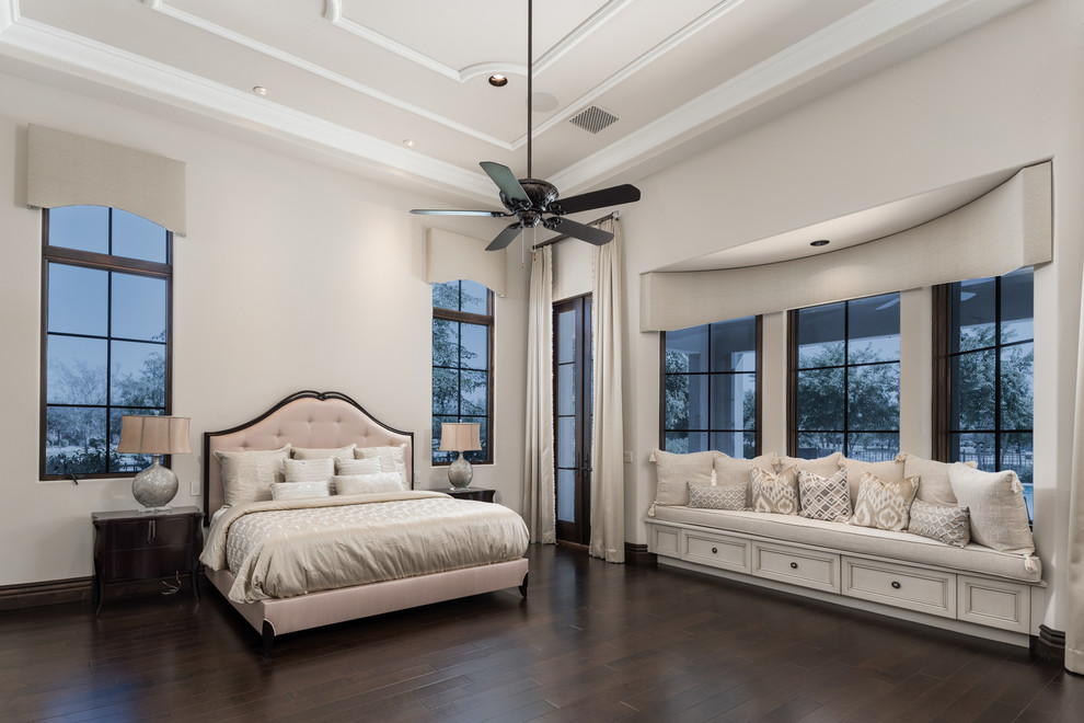 フェニックスにある巨大な地中海スタイルのおしゃれな主寝室 (ベージュの壁、濃色無垢フローリング、標準型暖炉、石材の暖炉まわり、茶色い床、三角天井) のレイアウト
