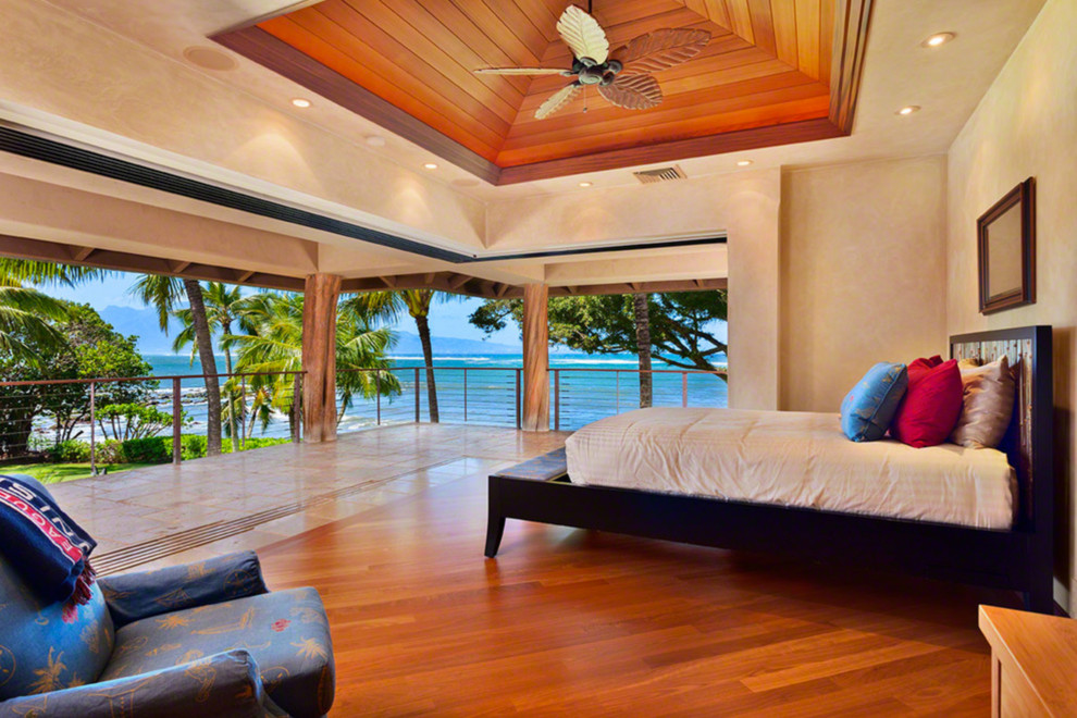 Ispirazione per una grande camera matrimoniale tropicale con pareti beige, pavimento in legno massello medio e pavimento marrone