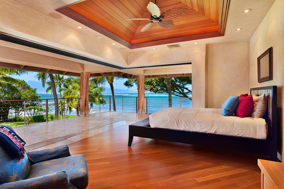 Diseño de dormitorio principal tropical grande sin chimenea con paredes beige, suelo de madera en tonos medios y suelo marrón