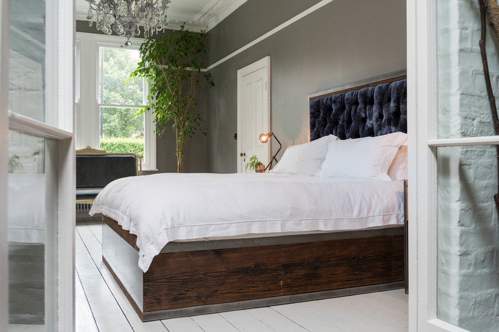 Cette image montre une grande chambre parentale minimaliste avec un mur gris, parquet peint, un poêle à bois, un manteau de cheminée en bois et un sol blanc.