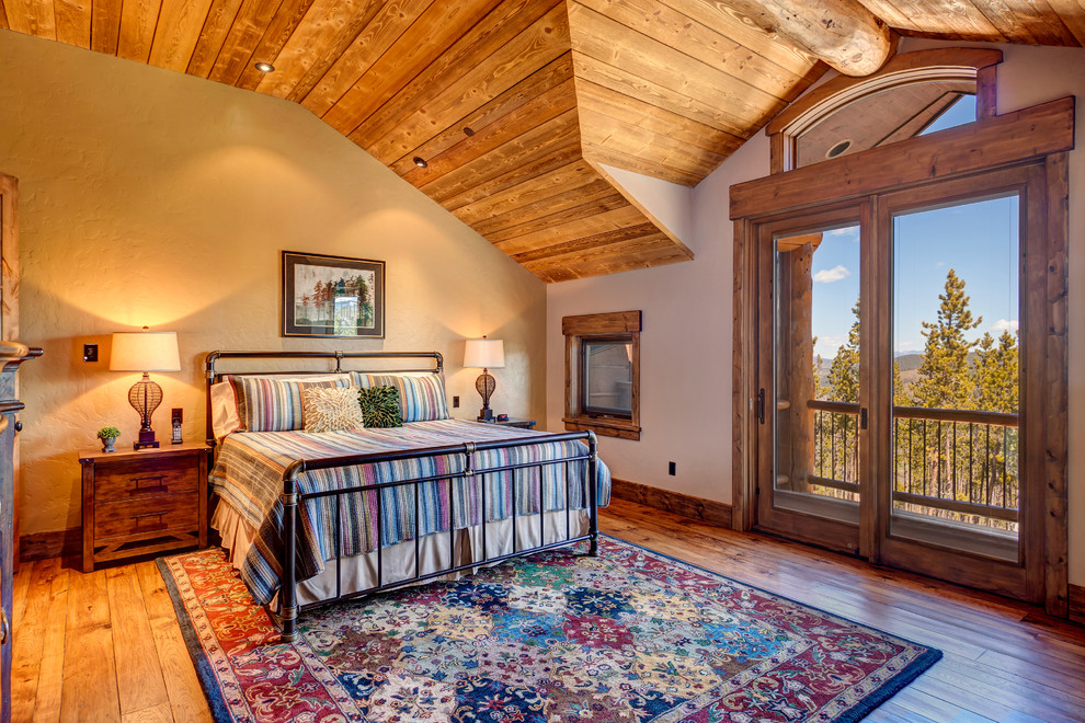 Imagen de dormitorio principal rural grande con paredes beige, suelo de madera en tonos medios, suelo marrón, todas las chimeneas y marco de chimenea de piedra