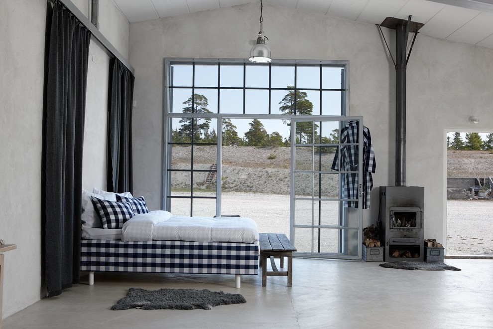 Immagine di un'ampia camera matrimoniale minimalista con pareti bianche, pavimento in cemento, stufa a legna e cornice del camino in metallo